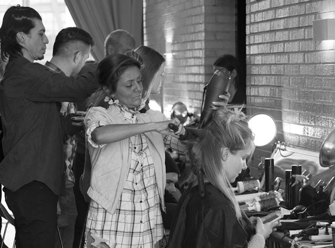 PANYC stylists style a seated model's hair with a round brush and dryer backstage, shot in black and white.