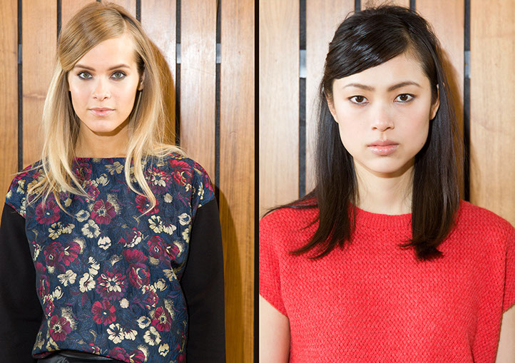 Two models backstage at Mercedes-Benz Fashion Week, one in a floral top and one in a red knit top, ready for the runway.
