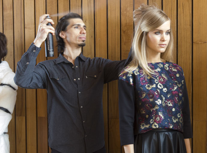 A PANYC stylist finishes a model's swept-back hairstyle with hairspray backstage.