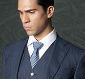 Black-and-white portrait of a male model with slicked side-parted hair, wearing a patterned tie and pinstripe vest