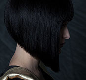 Profile of a sleek, graduated black bob with a blunt fringe, model wearing a gold-shouldered top