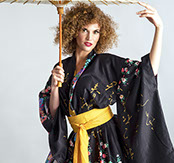 Model with a curly strawberry-blonde afro, posed under a paper parasol in a black kimono with a gold obi